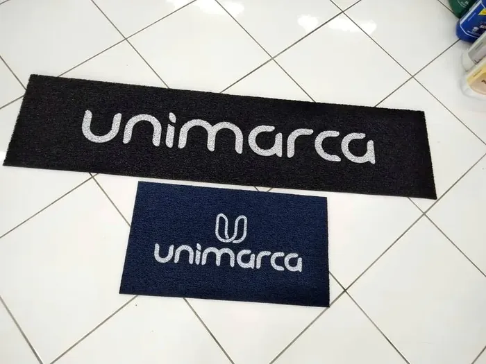 Dois tapetes de nylon com a logo Unimarca, um preto comprido e um azul menor