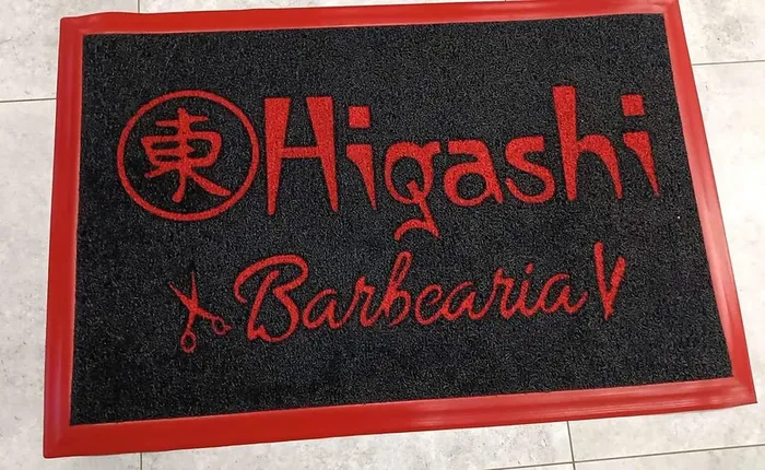 Capacho de vinil preto com borda pintada de vermelho e a logo da Higashi Barbearia