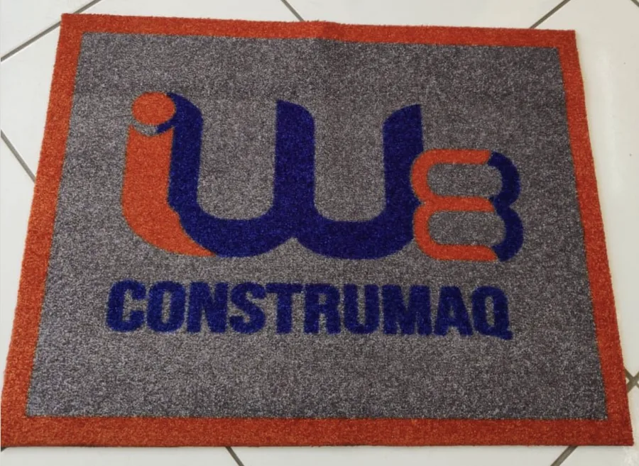 Tapete de nylon sintético cinza com borda pintada de laranja e a logo da Construmaq