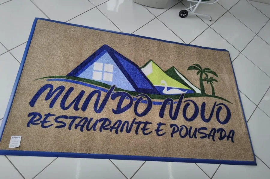 Tapete de nylon sintético bege com borda flex azul e a logo do Mundo Novo Restaurante e Pousada